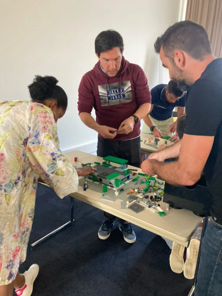 Défi LEGO Montréal équipes debout autour de tables de construction salle lumineuse · INNOV'events